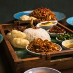 A vibrant Indonesian meal with rice, noodles, and various side dishes served in a wooden tray.
